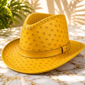 Peut inclure: Un chapeau fedora jaune vif présentant un motif texturé distinctif composé de petits points sombres régulièrement espacés sur toute la surface. Le chapeau comprend une bande jaune assortie entourant la base de la calotte et un bord large.