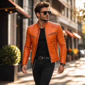 May include: A bright orange leather jacket with a textured crocodile skin pattern, featuring a stand-up collar, silver-tone metal zippers on the front pockets, and a central zipper closure, worn over a plain black t-shirt and black trousers.