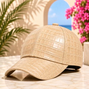 Peut inclure: Une casquette de baseball beige présentant un motif texturé en peau de crocodile sur toute la surface. La casquette possède une calotte structurée, une visière incurvée et un petit bouton au sommet, affichant un motif d'écailles en relief.
