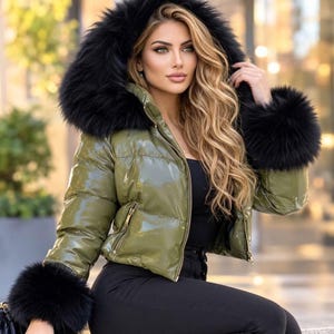 May include: A shiny olive green puffer jacket featuring a large black faux fur hood and matching black faux fur cuffs on the sleeves. The jacket has a front zipper closure with gold-toned hardware and horizontal quilted stitching throughout the body.