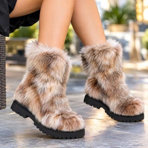Könnte beinhalten: Ein Paar wadenhohe Stiefel, die mit dickem, mehrfarbigem Kunstfell in Braun-, Beige- und Cremetönen bedeckt sind. Die Stiefel haben eine abgerundete Zehenpartie und eine klobige, schwarze Gummisohle mit tiefem Profil für besseren Halt.