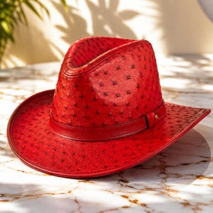 Peut inclure: Un chapeau de cowboy rouge vif présentant une surface texturée distincte avec des indentations sombres en forme de plumes, régulièrement espacées. Le chapeau comprend une bande en cuir rouge assortie autour de la base de la calotte.