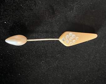 May include: A vintage brooch with a pearlescent white teardrop shape on one end and a light brown arrowhead shape with clear rhinestones on the other end.