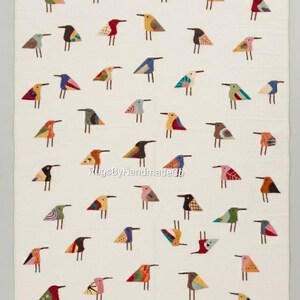 May include: A rectangular off-white rug featuring a repeating pattern of small, stylized birds in various colors including red, blue, yellow, green, and brown. The text RugsByHandmadeCo is printed in the center of the rug in a light gray font.