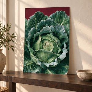 Op de afbeelding: Een rechthoekige wandkunstprint met een gedetailleerde illustratie van een grote, levendig groene kool met prominente, getextureerde bladeren. De kool is geplaatst tegen een effen, diepbordeauxrode achtergrond, wat de ingewikkelde witte nerven benadrukt.
