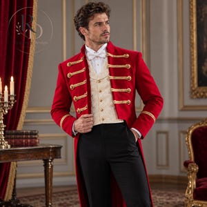 May include: A red tailcoat jacket featuring gold braided cord trim and gold buttons, worn over a cream-coloured patterned waistcoat with a white dress shirt, a white bow tie, and black trousers. The jacket has long sleeves with gold trim at the cuffs.
