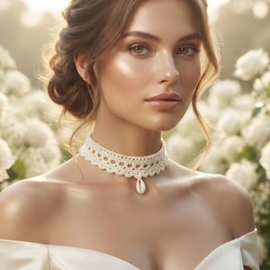 May include: A cream-colored crochet choker necklace featuring a delicate scalloped edge pattern and a single white cowrie shell pendant centered at the base, worn against a backdrop of white roses and baby's breath flowers in a garden setting.