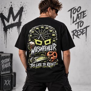 May include: A black short-sleeve t-shirt featuring a graphic on the back with a Ferris wheel, a beer mug, and a pretzel. The text reads WIESNFEHLER and TOO LATE TO RESET in white and yellow lettering against a dark background with green accents.
