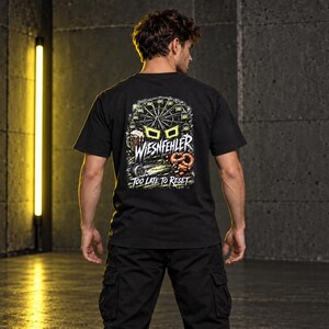 May include: A black short-sleeve t-shirt featuring a graphic on the back with a Ferris wheel, a beer mug, and a pretzel. The text reads WIESNFEHLER and TOO LATE TO RESET in white and yellow lettering against a dark, detailed background illustration.
