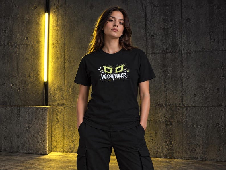 May include: A black short-sleeved t-shirt featuring a graphic print on the chest. The design includes two lime green rectangular shapes resembling eyes above the white text WIESNFEHLER, which is stylized with a distressed, jagged font effect.