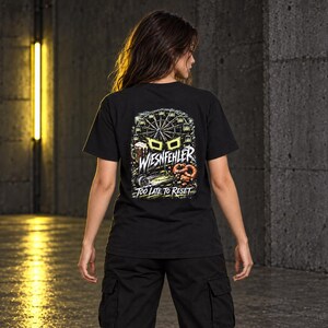May include: A black short-sleeve t-shirt featuring a graphic on the back with a Ferris wheel, a beer mug, and a pretzel. The text reads WIESNFEHLER and TOO LATE TO RESET in white and yellow lettering against a dark, detailed background illustration.