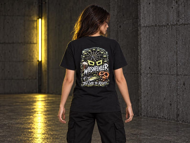 May include: A black short-sleeve t-shirt featuring a graphic on the back with a Ferris wheel, a beer mug, and a pretzel. The text reads WIESNFEHLER and TOO LATE TO RESET in white and yellow lettering against a dark, detailed background illustration.