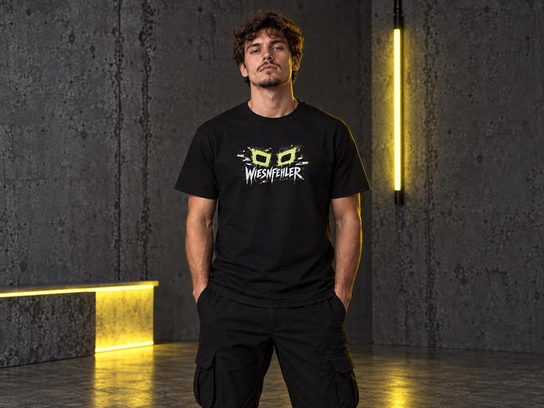 May include: A black short-sleeved t-shirt featuring a graphic print of lime green stylized glasses above the white text WIESNFEHLER. The design includes white paint splatter accents surrounding the glasses and text on the chest area.