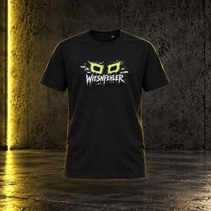 May include: A black short-sleeved t-shirt featuring a graphic on the chest with two lime green rectangular shapes above the white text WIESNFEHLER, which is stylized with a distressed, paint-splatter effect across the center of the garment.
