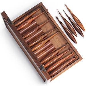 May include: A set of dark brown wooden crochet hooks with varying tip sizes, ranging from 6.00 mm to 15.00 mm, organized within a matching rectangular wooden storage case featuring metal hinges and a clear lid for viewing the contents inside.