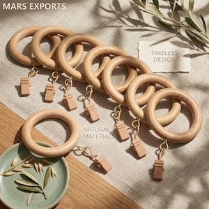 Può includere: Un set di anelli per tende in legno chiaro con clip metalliche attaccate. L'immagine include il testo MARS EXPORTS, TIMELESS DESIGN e NATURAL MATERIALS. Gli anelli sono disposti in fila con un anello separato posizionato sotto.