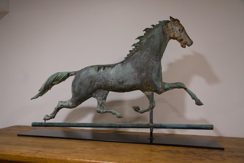 May include: A green metal horse sculpture with a long tail and mane, running on a black metal base. The horse is mounted on a long, thin metal rod.