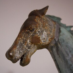 May include: Close-up of a weathered bronze horse sculpture with a detailed face and mane. The sculpture has a green patina and shows signs of age.