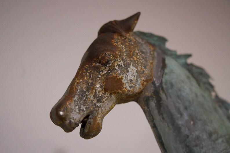 May include: Close-up of a weathered bronze horse sculpture with a detailed face and mane. The sculpture has a green patina and shows signs of age.