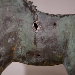 May include: A close-up of a bronze sculpture of a horse with several holes in its side. The sculpture is weathered and has a green patina.