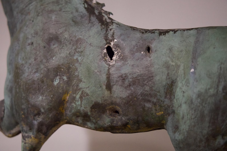 May include: A close-up of a bronze sculpture of a horse with several holes in its side. The sculpture is weathered and has a green patina.