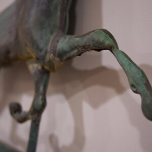 May include: A bronze horse sculpture with a green patina finish. The horse is in mid-stride with its legs raised. The sculpture is detailed with textured surfaces and a realistic appearance.