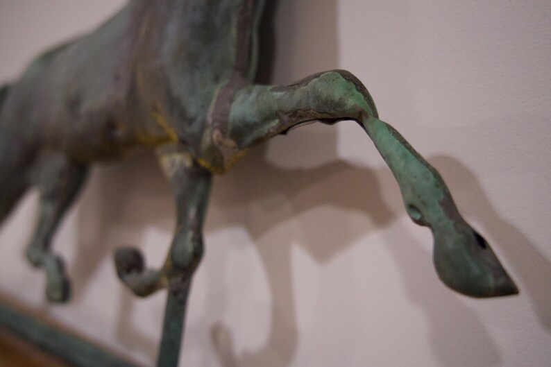 May include: A bronze horse sculpture with a green patina finish. The horse is in mid-stride with its legs raised. The sculpture is detailed with textured surfaces and a realistic appearance.