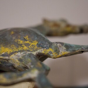 May include: A bronze sculpture of a horse with a green and yellow patina. The horse is lying down with its head turned to the side.