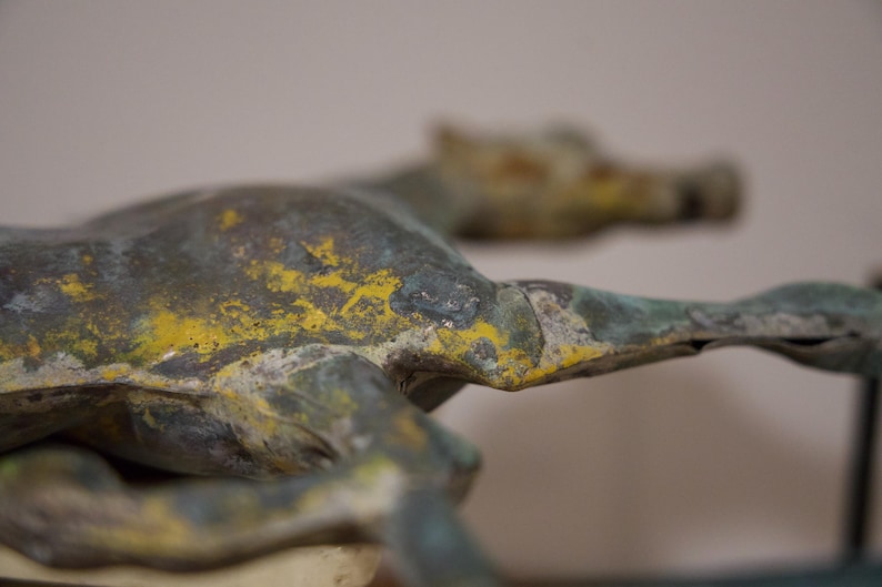 May include: A bronze sculpture of a horse with a green and yellow patina. The horse is lying down with its head turned to the side.