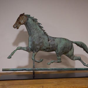 May include: A green metal horse weathervane with a long tail, standing on a black metal base. The horse is in a running pose with its head turned to the side.