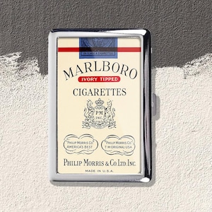 Może przedstawiać: Prostokątna papierośnica z chromu z grafiką w stylu vintage Marlboro Ivory Tipped z przodu. Projekt zawiera napis Marlboro, Cigarettes, Philip Morris & Co. Ltd. Inc. oraz Made in U.S.A. wraz z centralnym herbem i wizerunkiem lwów.