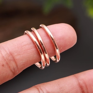 Può includere: Tre anelli in metallo lucido color oro rosa con un design semplice a fascia arrotondata. Gli anelli sono impilati insieme, mostrando una finitura metallica riflettente e una forma circolare liscia e uniforme senza pietre o incisioni.