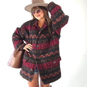 Peut inclure: Une veste à manches longues boutonnée présentant une base gris anthracite foncé avec un motif géométrique répétitif en rouge vif et orange brûlé. La veste comprend un col classique, deux poches à rabat avant et des boutons sur le devant.