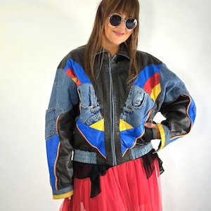 May include: A multi-colored jacket featuring a combination of black leather and blue denim panels. The design includes vibrant red and yellow accents, a front zipper closure, a standard collar, and a ribbed hemline at the waist and cuffs.