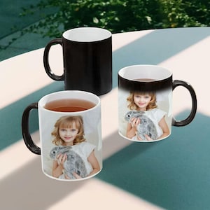 May include: Three black magic mugs with a white interior. The mugs have a photo of a child holding a rabbit printed on them. The photo appears when the mug is filled with a hot beverage.