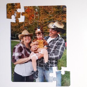 May include: A family portrait printed on a puzzle. The image shows a family of three, with the child in a horse costume. The parents are wearing cowboy hats and plaid shirts. The background features autumn foliage.
