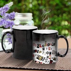 May include: Two black ceramic mugs with white interiors. One mug is blank, the other has a design of words in red, black, and yellow on a white background. The words include "Evolutionary", "Hype", "Exceptional", and "Impressive".