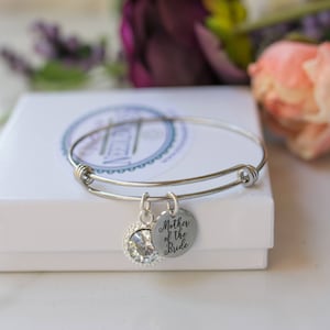 May include: A silver expandable bangle bracelet with a charm that says "Mother of the Bride" and a clear crystal charm.