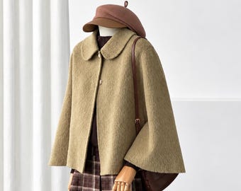 May include: A tan textured cape jacket with a rounded collar and front buttons, worn over a dark brown turtleneck and a brown plaid pleated skirt. A brown beret and a brown shoulder bag with a thin strap complete the ensemble.