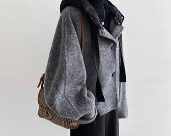 May include: A grey fuzzy hooded jacket with a black turtleneck underneath, featuring two front buttons and long sleeves. A brown and black plaid shoulder bag with a leather strap is worn over the shoulder, paired with black trousers.