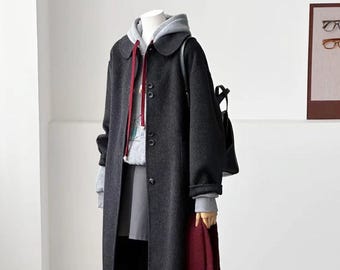 May include: A charcoal grey wool-blend coat with a rounded collar and button front, layered over a light grey hooded sweatshirt with red drawstrings. Includes a dark grey skirt, a maroon scarf, a black backpack, and dark brown shoes with white socks.