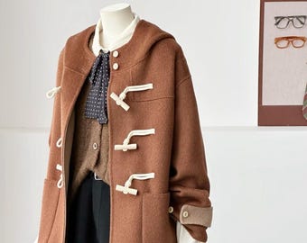 May include: A brown hooded coat featuring white toggle fastenings, long sleeves with buttoned cuffs, and two front patch pockets. The coat is layered over a white collared shirt, a brown knit cardigan, a black polka-dot necktie, and black shorts.