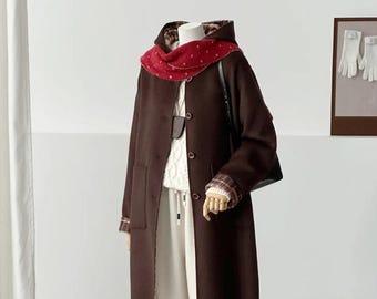 May include: A dark brown hooded coat with a button-front closure, worn over a white cable-knit jumper and cream-coloured wide-leg trousers. The outfit includes a red scarf with white dots, plaid sleeve cuffs, and tan slip-on ankle boots.