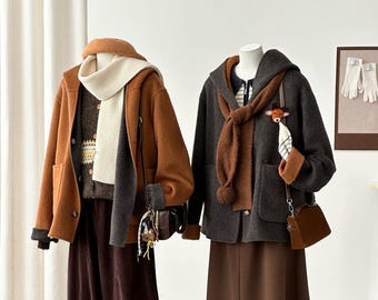 May include: Two mannequins display layered autumn outfits. The left features a tan hooded coat, cream scarf, patterned jumper, and dark brown trousers. The right wears a charcoal hooded coat, brown scarf, striped shirt, brown skirt, and tan slippers.