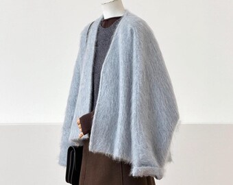 May include: A light blue fuzzy open-front cardigan layered over a dark grey sweater and a dark brown skirt. The outfit is completed with a small black handbag held at the side. The garments are displayed on a mannequin against a plain background.
