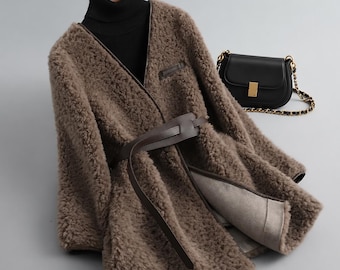 May include: A brown faux shearling coat with a dark brown leather belt, worn over a black turtleneck sweater. A small black leather handbag with a gold clasp and a gold chain strap is positioned next to the coat on a hanger.