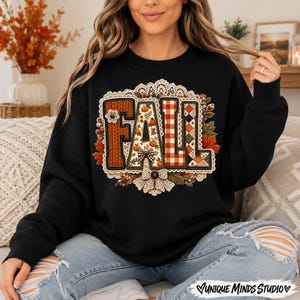 May include: A black long-sleeve sweatshirt featuring a large graphic on the chest that spells the word FALL. The letters are decorated with patterns of orange pumpkins, red and white gingham, and knit textures, all framed by a cream lace border.