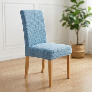 May include: A dining chair featuring a light blue stretch fabric cover with a textured, woven-look geometric pattern. The chair has a high backrest and four straight, light-toned wooden legs, providing a stable base for the upholstered seat.