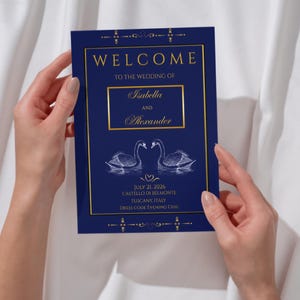 May include: A rectangular wedding welcome sign in deep navy blue with gold borders and text. It features the names Isabella and Alexander, a white illustration of two swans facing each other, and the date July 21, 2026, at Castello di Belmonte.