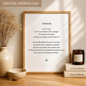 May include: A framed wall art print featuring the title STRANGER in black text, followed by a poem about human interaction and the power of love, ending with three small stars. The print is displayed in a light wood frame on a wooden surface.